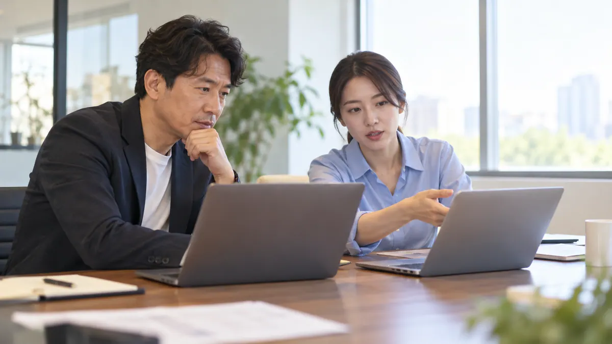 회의실에서 사장님과 담당자가 노트북 두 대를 나란히 놓고 예전 화면과 새 화면 구성을 비교하는 기획 이미지
