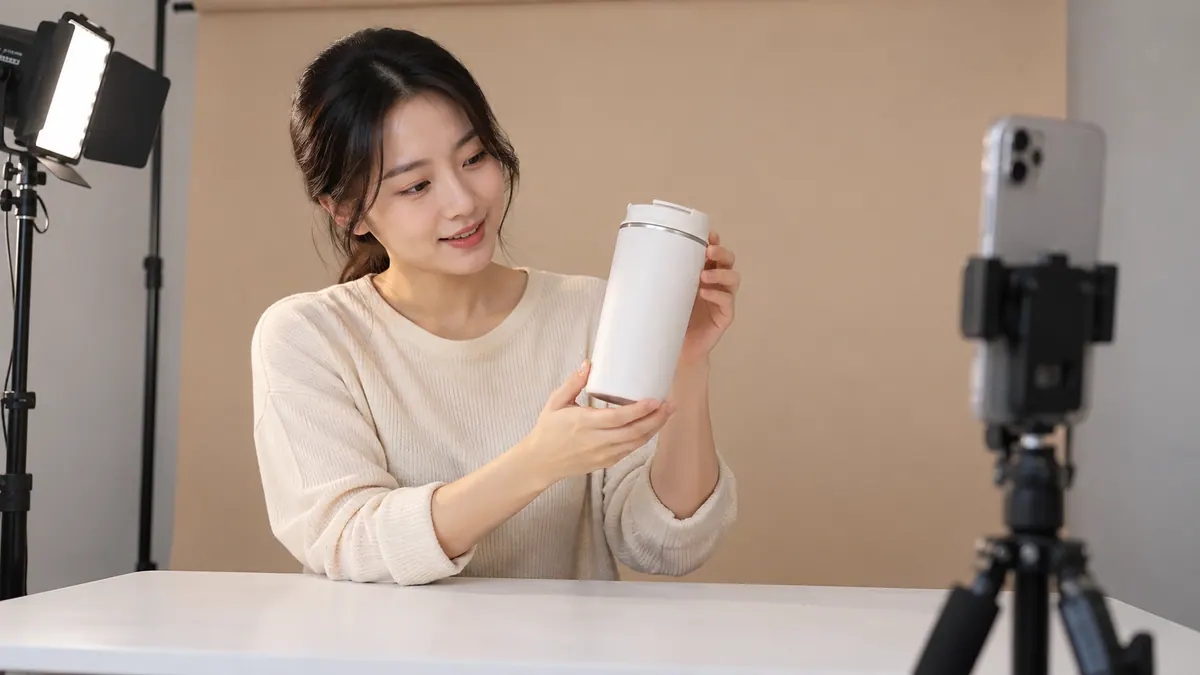 작은 촬영 공간에서 판매자가 휴대폰을 세로로 세워 두고 탁자 위 상품을 짧게 촬영하는 기획 이미지
